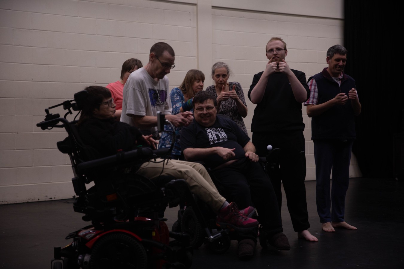In My Younger Years – rehearsal in the section 'Computer Games':  Jen-Jo Bartholemew-Biggs, David Bartholemew-Biggs, Arlene James, Agnieszka Michalik, Karen Rush, Sam Cleeton, Sam Evans, and in the front, Eddie Wadsworth. Eight persons in casual clothes: five are standing, and two are sitting in wheelchairs. They all act as if they were playing a console game.