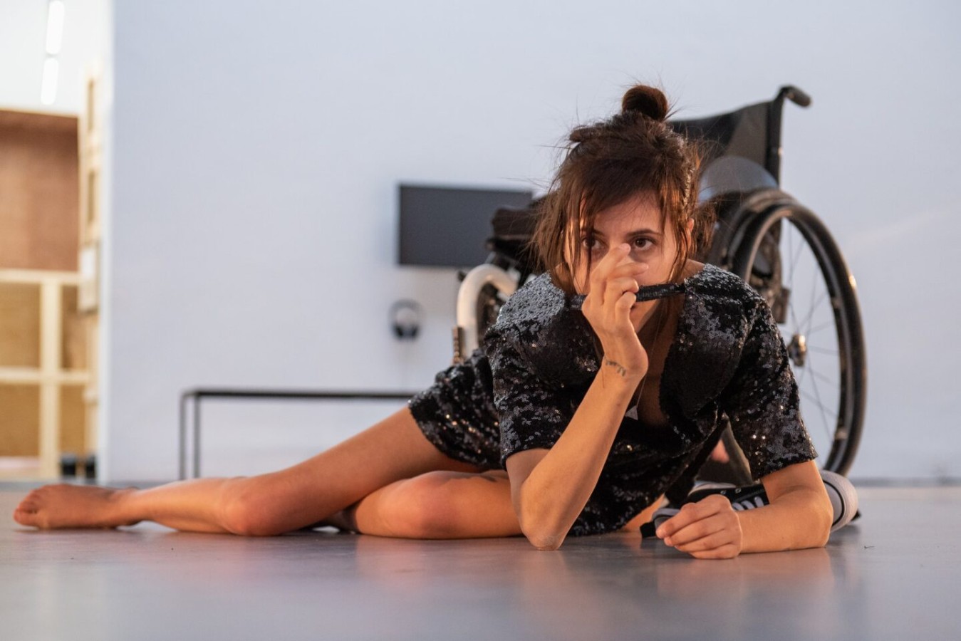 Teatr 21, PokaZ: Diana Niepce. Diana Niepce leży na jasnej podłodze. Tułów i głowę unosi na opartych o ziemię rękach. Twarz częściowo zasłania dłonią. Jej póługięte, nagie nogi leżą na podłodze. W tle widać fragmenty wózka i białą salę galeryjną.  